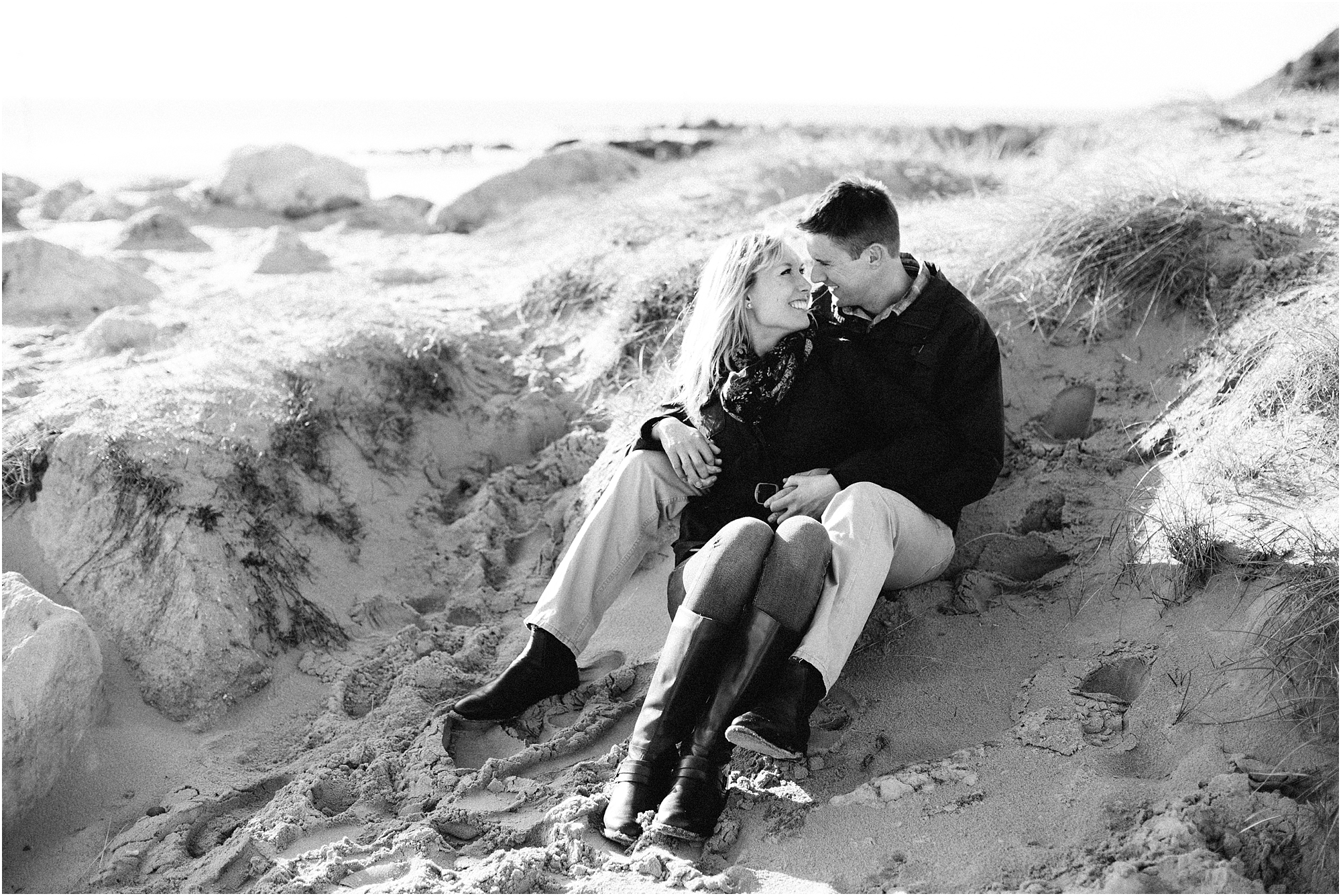 Black and white photo of couple sitting in sand dunes