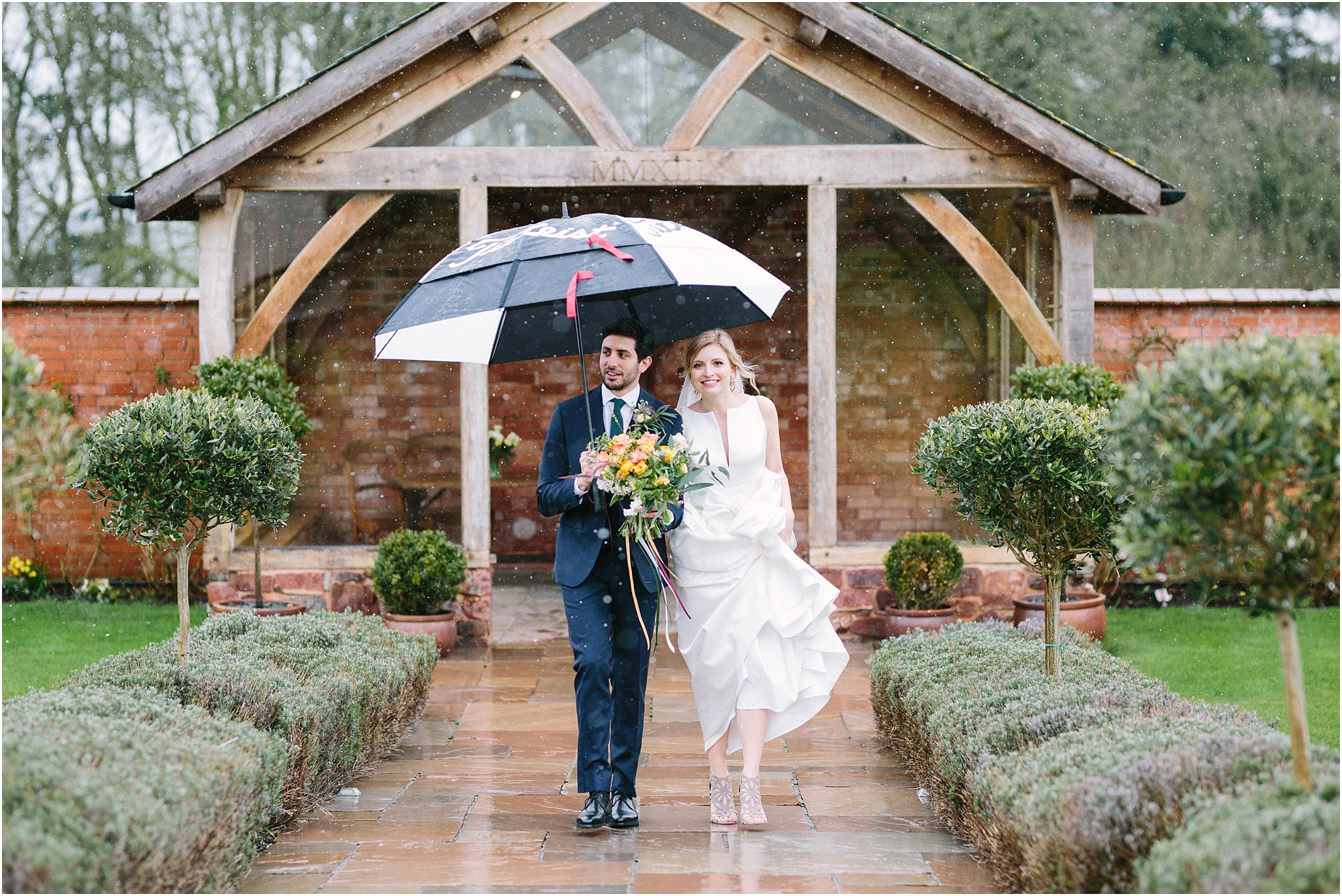 Bride and groom walking with umbrella at Upton Barn Wedding Venue