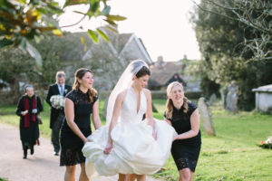 Bride walking to Boxgrove Priory holding up her wedding dress