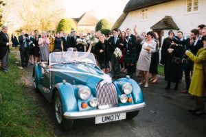 Bride and groom leaving Boxgrove Priory in blue convertible vintage wedding car