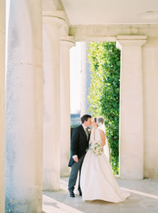 Bride and groom kissing under the pillars of Goodwood House wedding