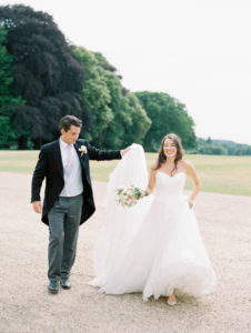 Groom holding brides train of dress as they walk