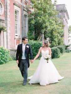 Bride and groom walking hand in hand in the ground of Stansted House