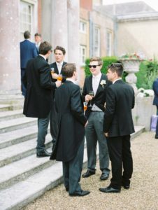 Elegant male wedding guests talking on the steps of Stansted House