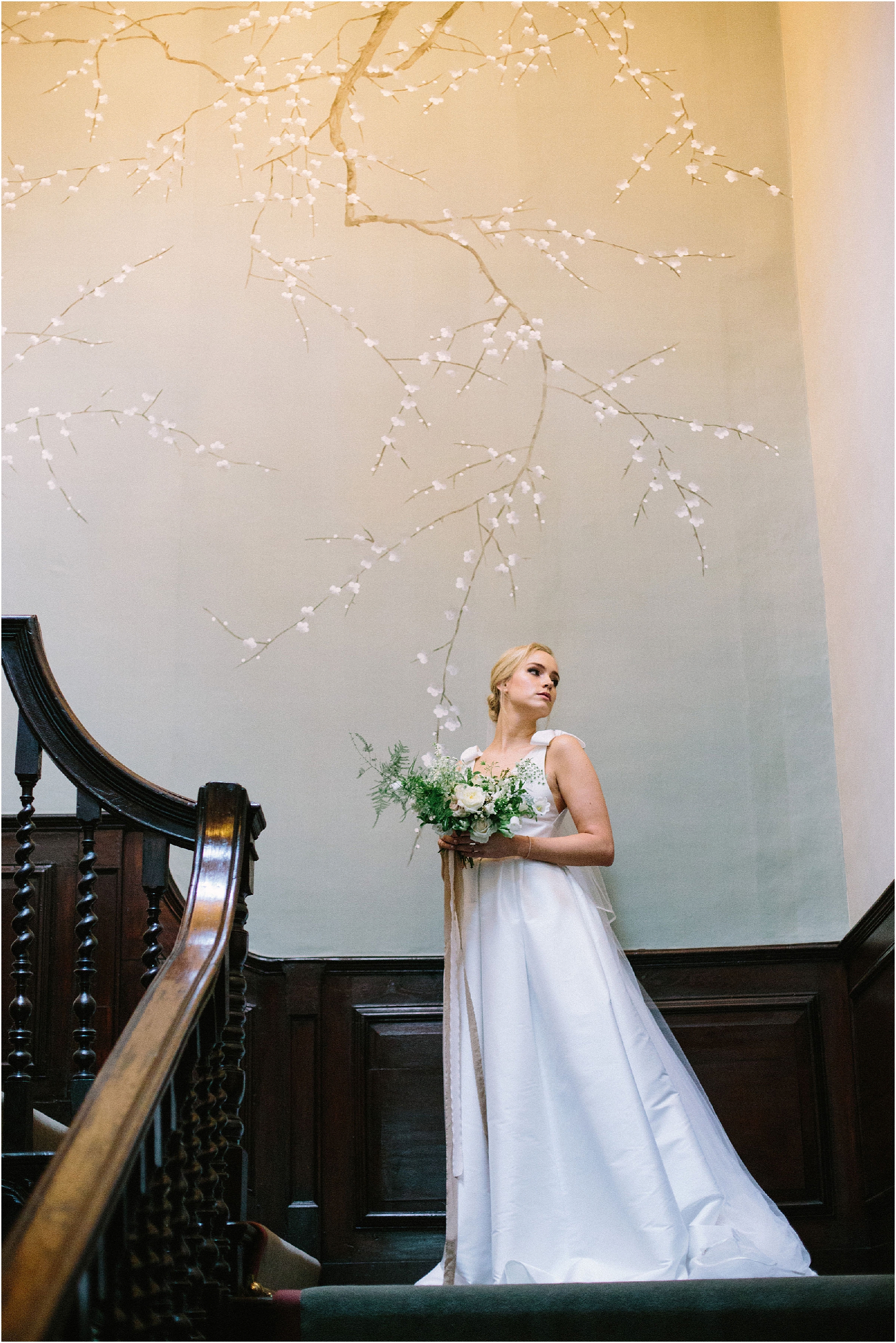 Bride standing on the staircase in front of silk hand painted wallpaper at Thorpe Manor