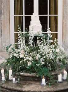 Cream five tier wedding cake amongst floral display on the steps of Thorpe Manor