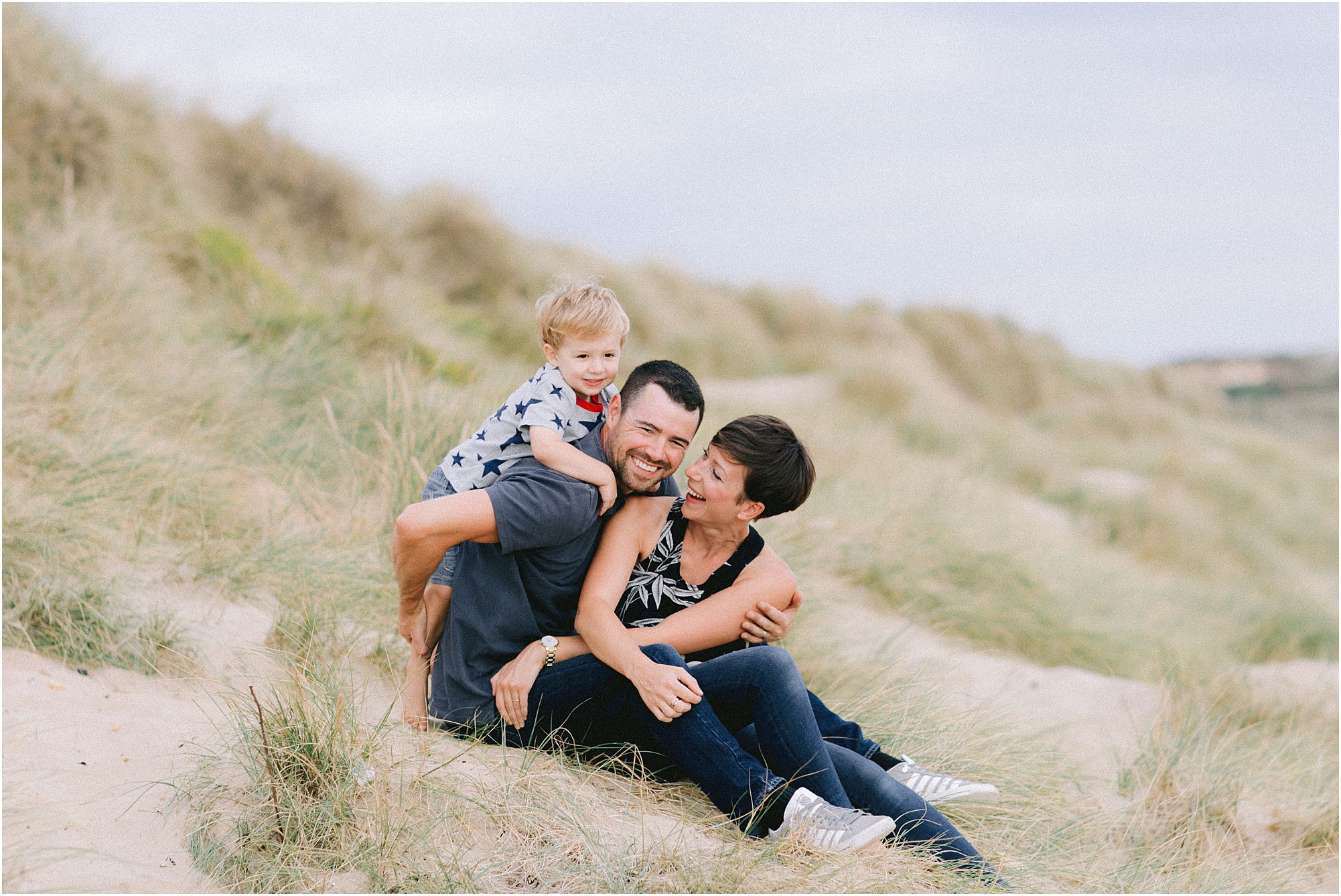 Family of three sitting on sand dune laughing