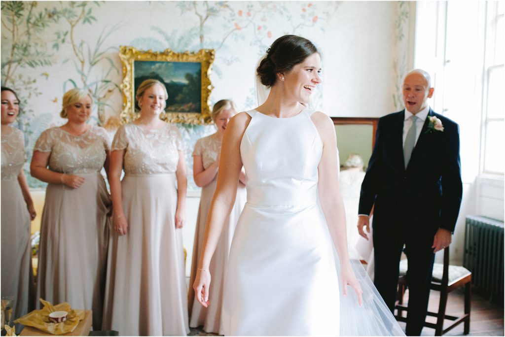 Bride with father of bride and bridesmaids revealing wedding dress