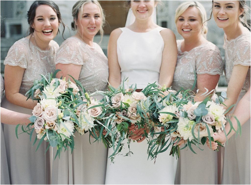 Bride and bridesmaids holding bouquets of roses and eucalyptus