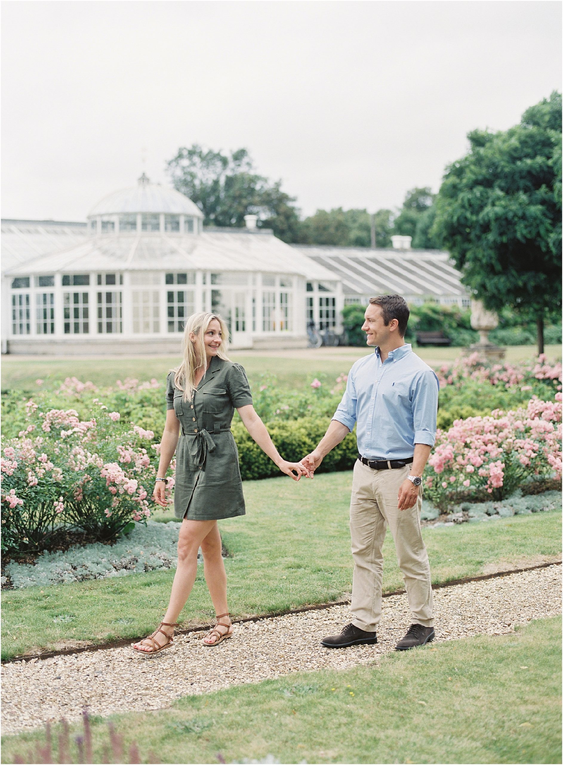 Newly engaged couple walking hand in hand in rose garden