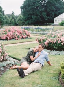 Newly engaged couple sitting on the grass in rose garden