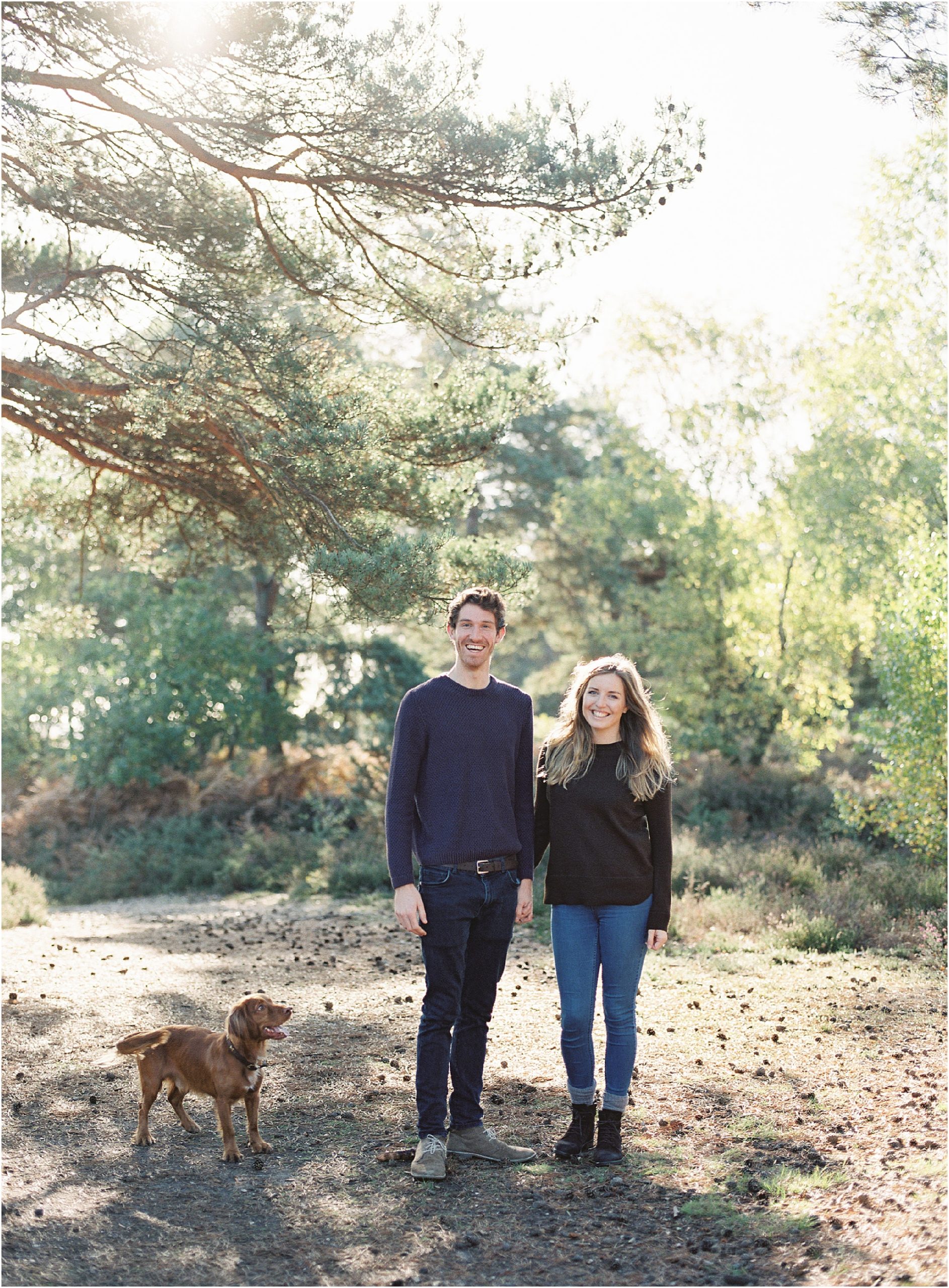 Engaged couple with their dog smiling at the camera. Captured on film by Camilla Arnhold Photography