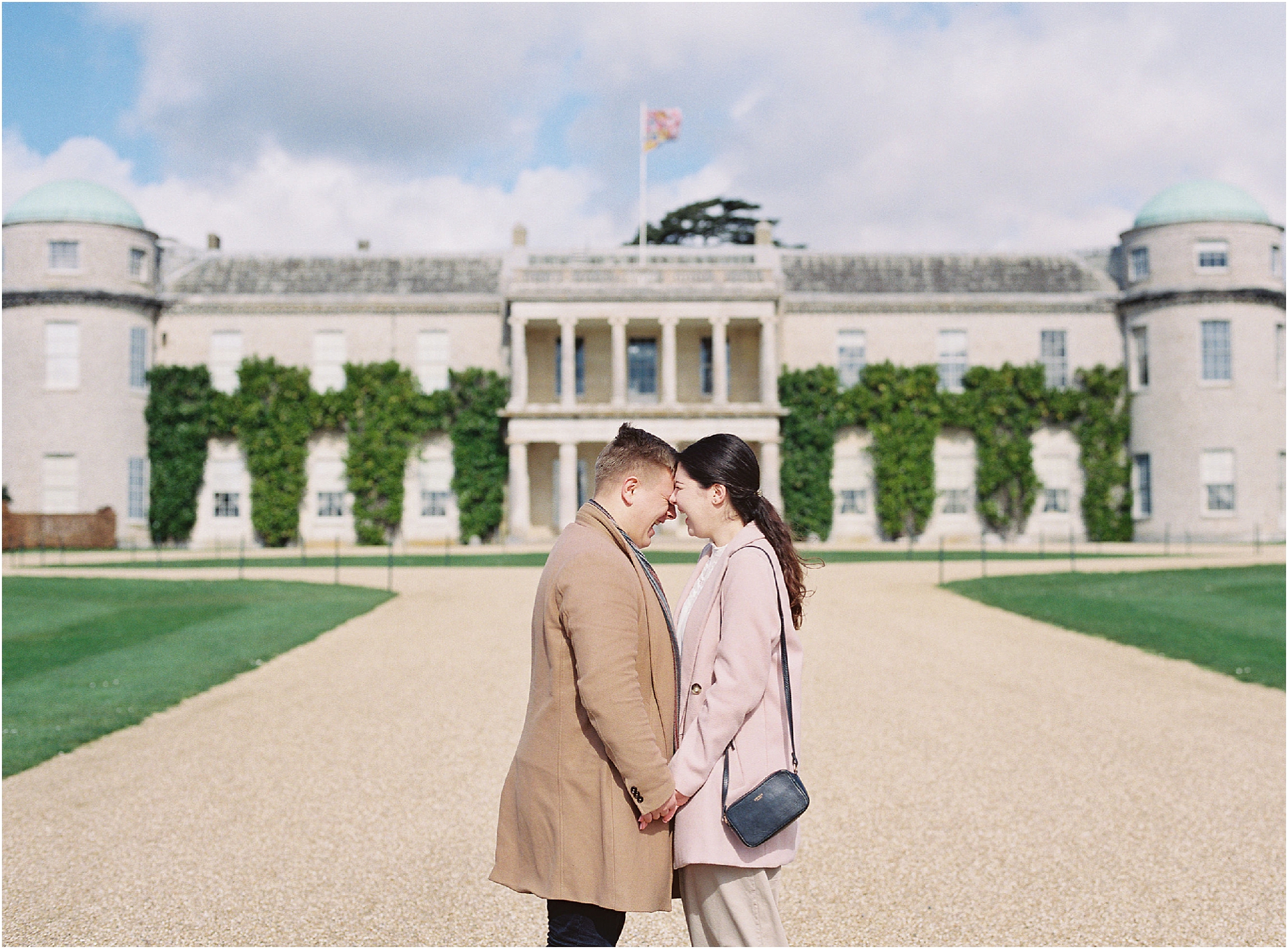 Couple laughing in front of Goodwood House Sussex on their engagement shoot