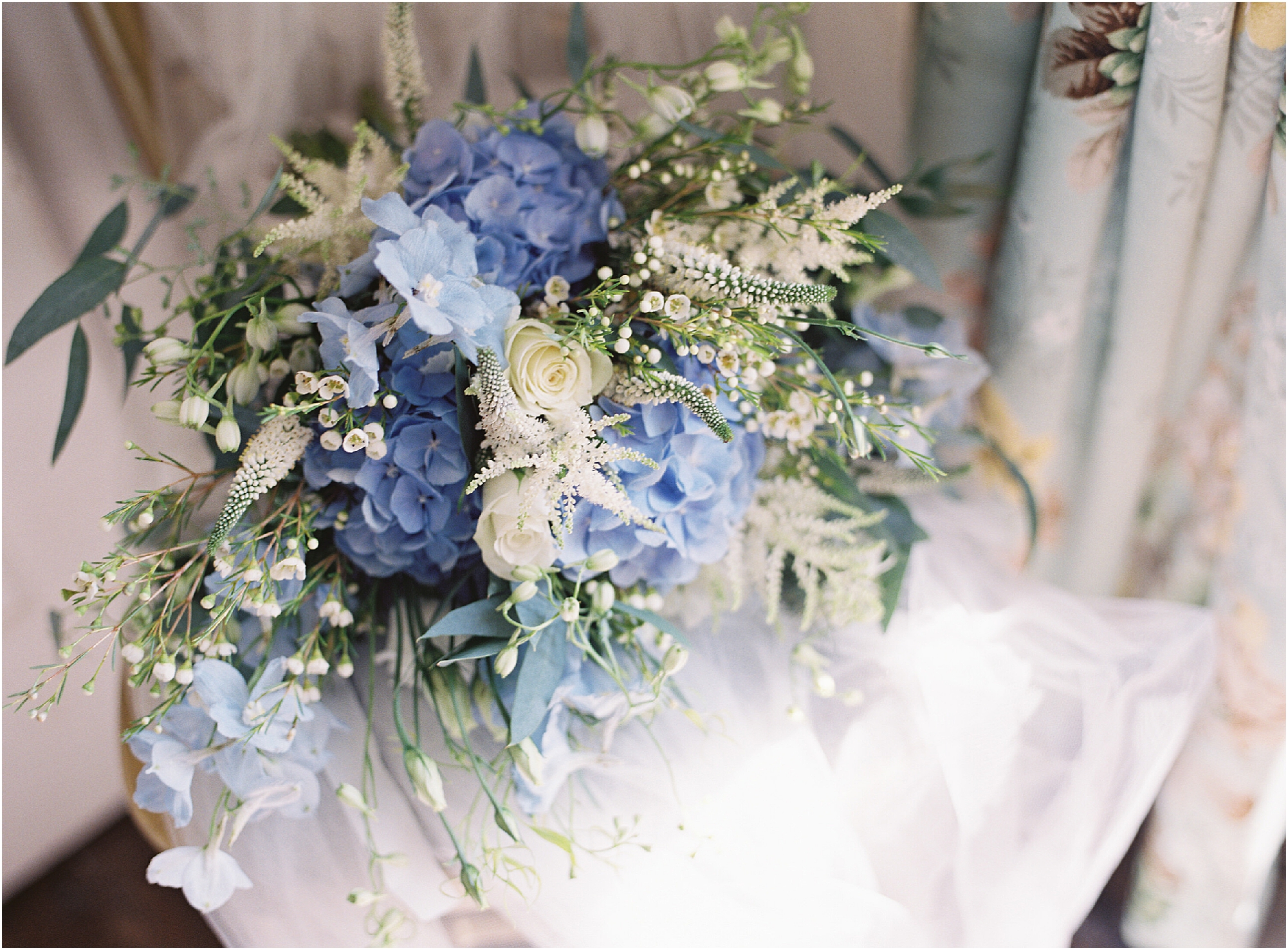 Blue and white bridal bouquet laying on a chair with wedding veil
