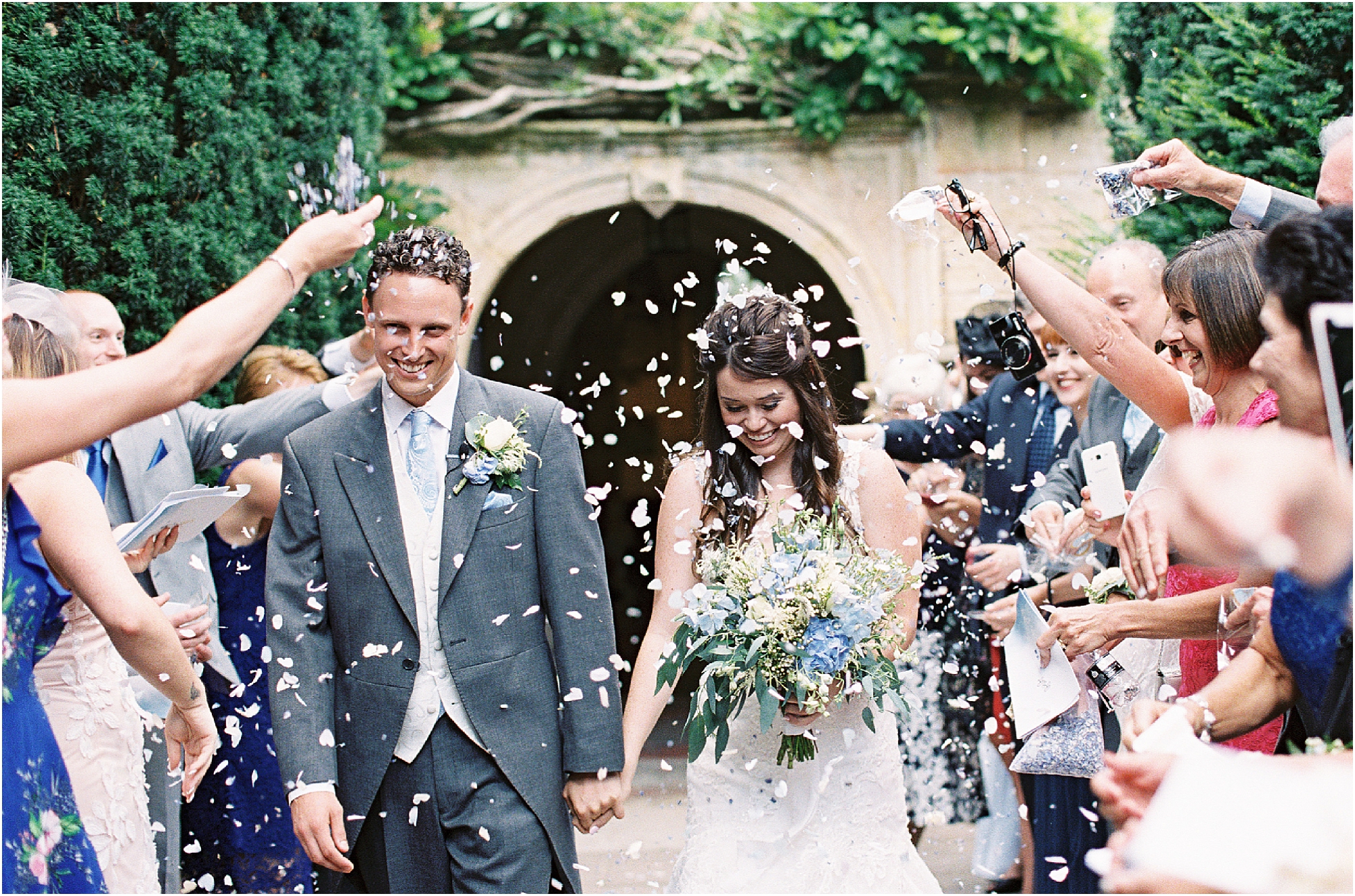 Bride and groom walking through confetti smiling after wedding ceremony photography at Chiddingstone church