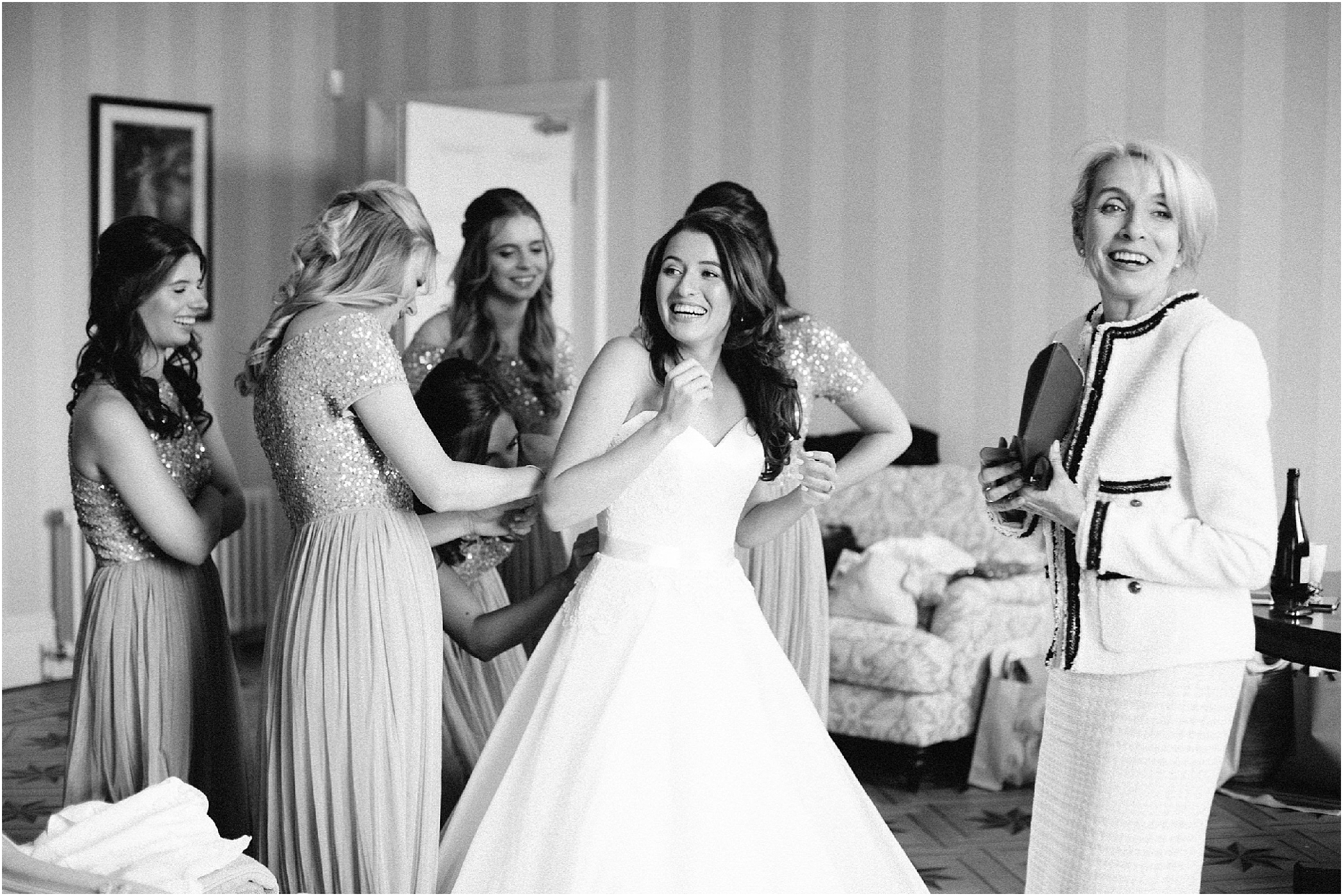 Bride with mother and bridesmaids putting on wedding dress in bridal suite